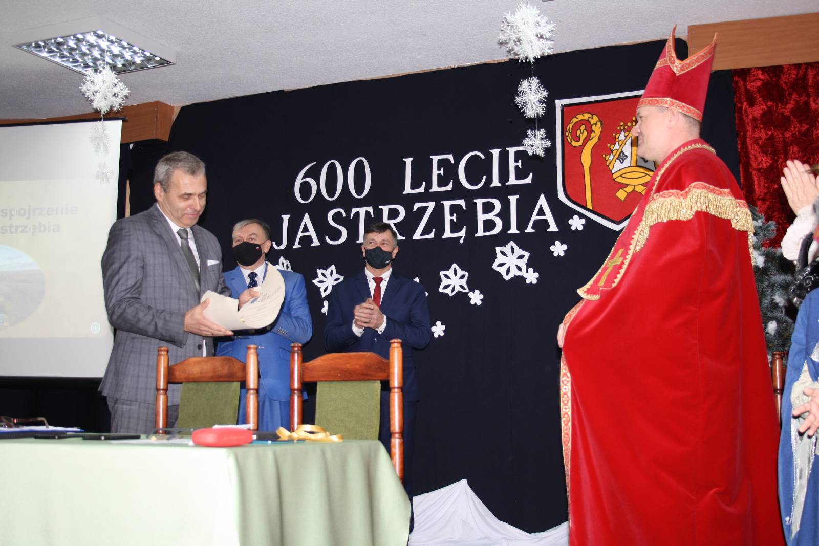 Wójt Gminy Jastrząb, Przewodniczący i Wiceprzewodniczący Rady Gminy oraz osoba grająca Biskupa Wojciecha Jastrzębca czytająca akt założenia miejscowości Jastrząb, na tle tablicy z napisem 600 Lecie Jastrzębia