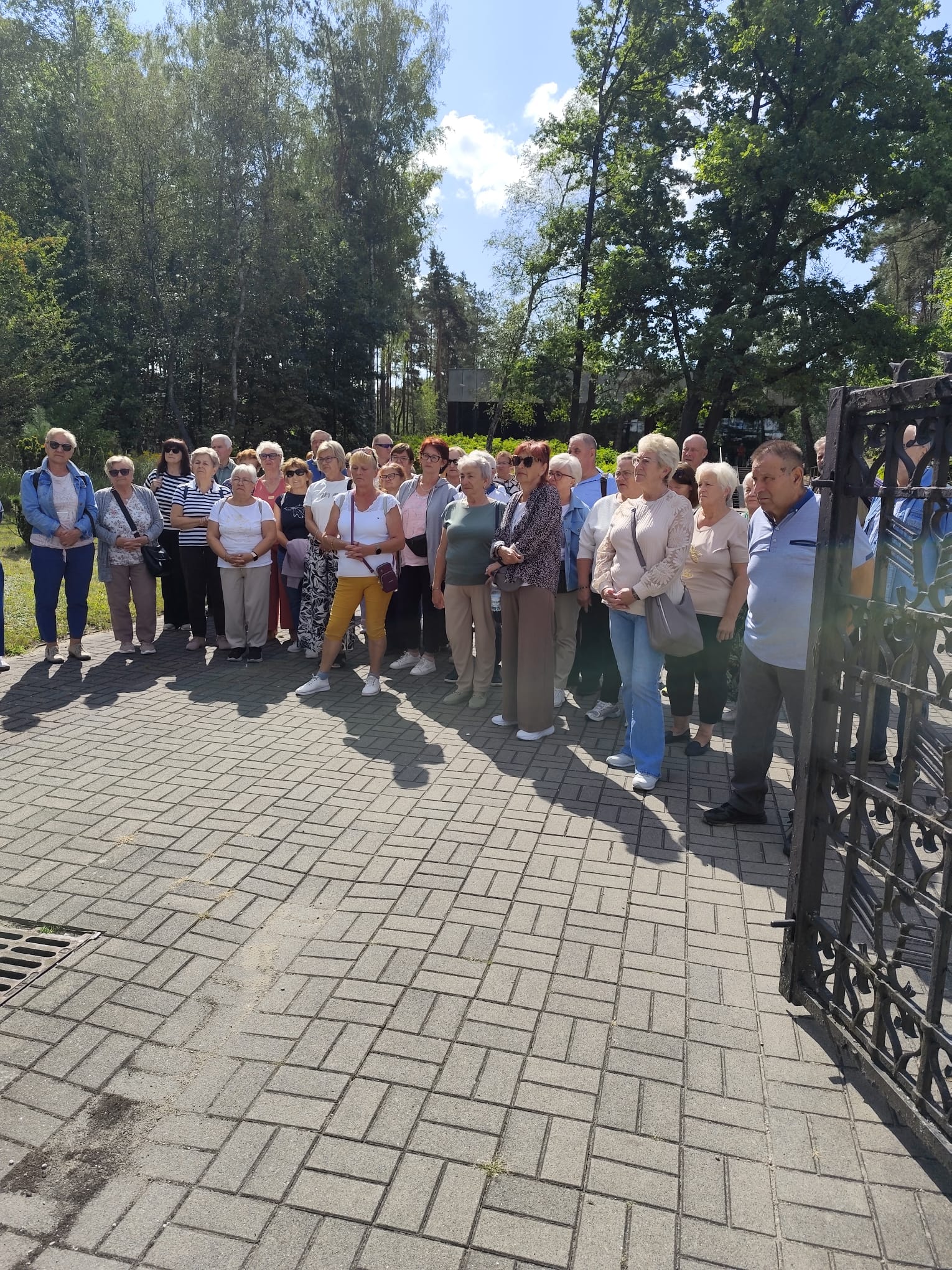 Zdjęcie grupowe, wykonane w pozycji wertykalnej, przedstawiające seniorów na tle lasu